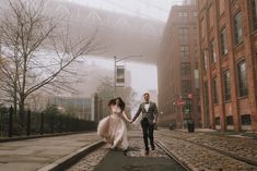 a bride and groom walking down the street holding hands in front of an overpass