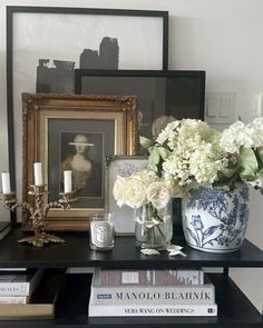 a black table topped with books and vases filled with flowers next to framed pictures