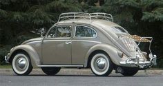 an old vw bug with a basket on the roof is parked in front of some trees