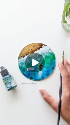 a person holding a paintbrush next to a cookie and some other items on a table