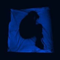 the silhouette of a person sitting in front of a blue light on a black background