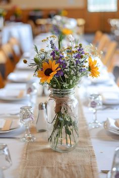 a mason jar filled with lots of flowers on top of a long dining room table