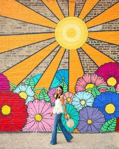 a woman standing in front of a colorful wall with flowers painted on it and holding a frisbee