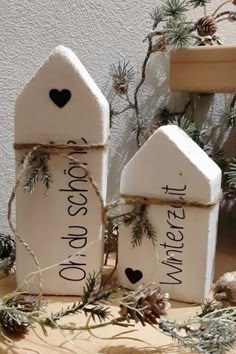 three small white houses with black hearts on them and pine cones in the foreground