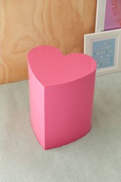 a pink heart shaped box sitting on top of a table next to two framed pictures