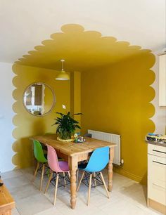 a dining room table with colorful chairs and a potted plant in the center, against a yellow wall