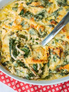 a casserole dish with spinach, cheese and chicken in it on a red and white checkered cloth