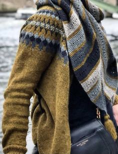 a woman wearing a yellow and gray sweater with a scarf around her neck is standing by the water