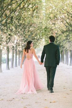 a man and woman holding hands while walking down a tree lined path in front of trees