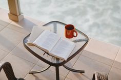 an open book sitting on top of a glass table next to a cup of coffee