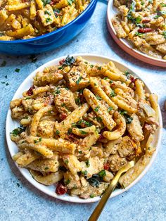 two plates filled with pasta and meat on top of a blue tablecloth next to bowls of food