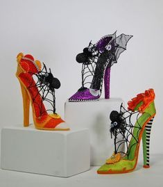 three pairs of high heeled shoes decorated with spider webs and skulls on white blocks