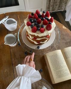 a person pointing at a cake on a table with an open book and cup of coffee