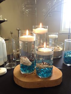 three candles are sitting in glass vases with rocks and seaweed on the table