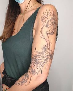 a woman wearing a face mask and holding her arm with a bird tattoo on it