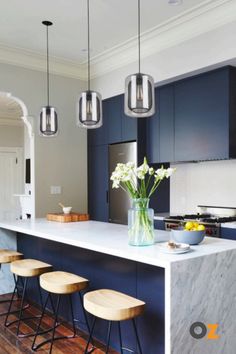 a kitchen with blue cabinets and marble counter tops, stools are in front of the island