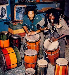 two men sitting next to each other in front of some musical instruments and drum heads