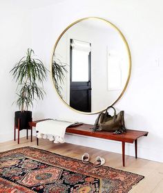 a large round mirror sitting on top of a wooden bench next to a rug and potted plant