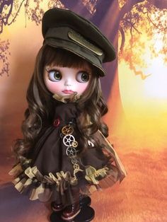 a doll with long hair wearing a brown dress and green hat, standing in front of a tree