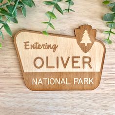 a wooden sign sitting on top of a table next to some leaves and plants in front of it