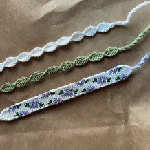 three crocheted bracelets with green and blue designs on them sitting on a piece of paper