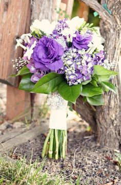 a bouquet of purple and white flowers sitting on the ground in front of a tree