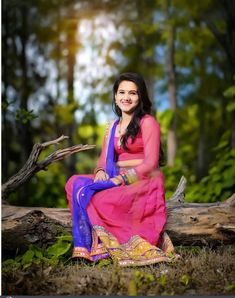 a woman in a pink and blue dress sitting on a tree branch with her arms crossed