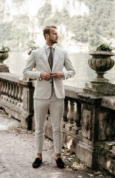 a man in a suit and tie standing on a bridge next to the water with his hands in his pockets