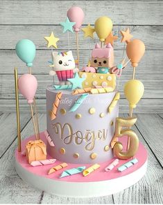 a birthday cake with balloons, stars and other decorations on the top is decorated in pastel colors