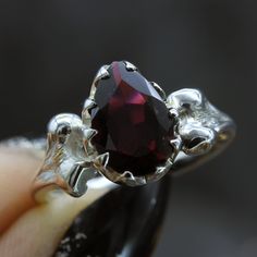 a woman's hand holding a ring with a large red stone in the middle