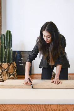 a woman cutting wood with a pair of scissors in front of a potted cacti