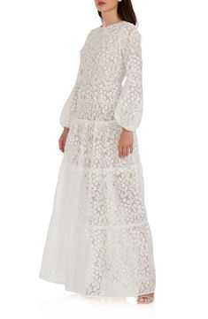 Radiate the beauty of a field of flowers in this gently swaying gown that features a sweeping peekaboo skirt and a breathtaking open back. 63" length (size Small) Jewel neck Long sleeves Partially lined 100% polyester Hand wash, line dry Imported Wedding Maxi Dress With Voluminous Skirt, White Dresses With Voluminous Skirt For Garden Party, Elegant Maxi Dress With Voluminous Skirt For Wedding, Feminine Wedding Dress With Voluminous Skirt, Voluminous Maxi Length Wedding Dress, Voluminous Maxi Dress For Wedding, White Voluminous Skirt Wedding Dress, Ethereal White Floor-length Gown, White Scalloped Lace Maxi Dress