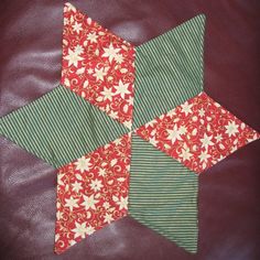 a red and green patchwork quilt with white stars on the top, sitting on a brown leather surface