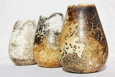 three vases sitting next to each other on a white tableclothed surface, one is gold and the other has black speckles