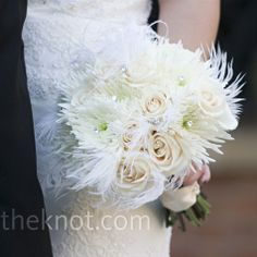 a close up of a bride holding a bouquet of white flowers and feathers on her wedding day