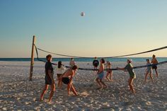 group of people playing volleyball on the beach with net in front of them at sunset