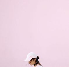 a woman with a tennis racquet standing in front of a pink wall wearing a white hat