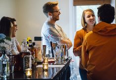 a group of people standing around a bar with drinks on the counter and liquor bottles in front of them