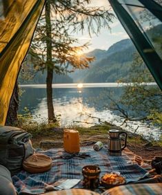 an open tent with food and coffee on the ground next to it, overlooking a body of water