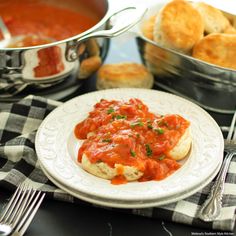 a white plate topped with bread covered in marinara sauce next to silver pans