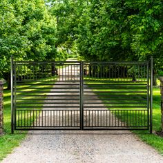 an iron gate in the middle of a path leading to a grassy area with trees