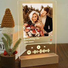 an illuminated photo frame on a table with a pine cone and christmas tree in the background