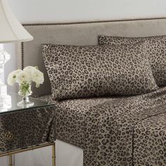 a leopard print bed spread with white flowers in a vase on a nightstand next to it