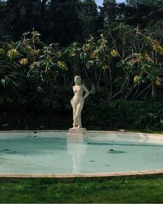 a statue in the middle of a pool surrounded by trees