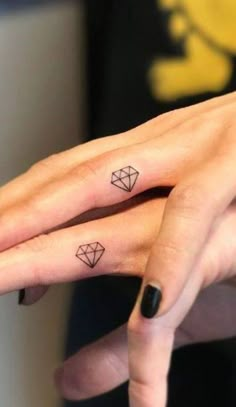 two fingers with small tattoos on them, one has a diamond and the other has a heart