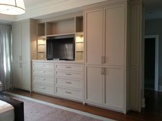 a living room with white furniture and a flat screen tv mounted on the cabinet doors