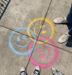 two people are standing on the sidewalk with their feet up and one is drawing smiley faces