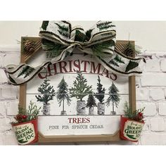 a wooden sign with christmas trees and pine cones hanging from it's sides, in front of a brick wall