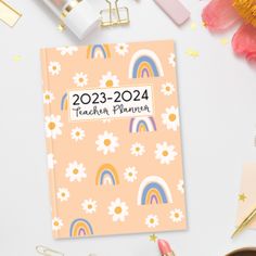 a pink planner with flowers and rainbows on it, surrounded by other office supplies