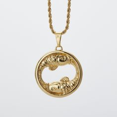 a gold necklace with two fish in the middle and an oval shaped pendant hanging from it's side